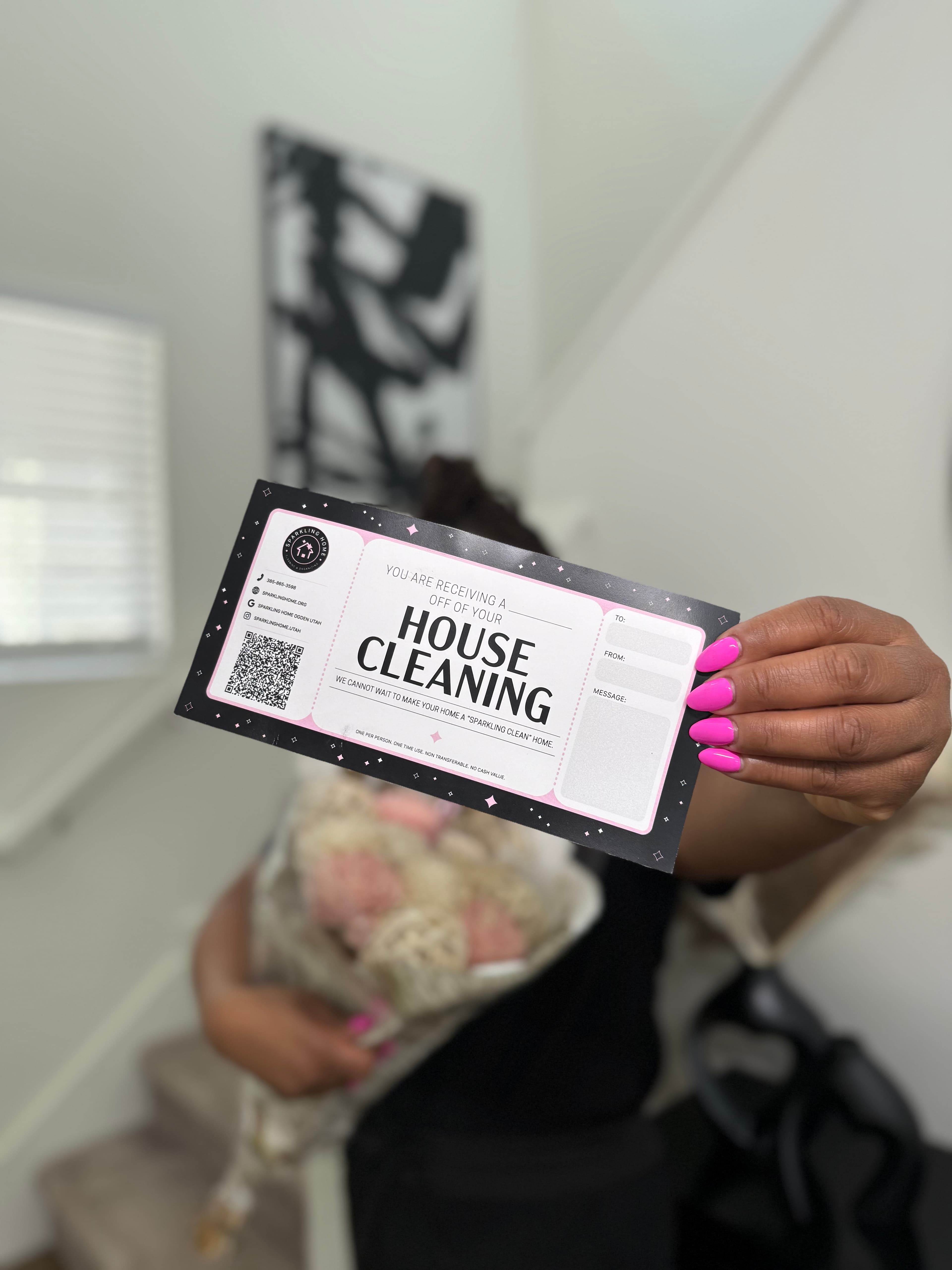Woman holding a house cleaning gift card and a bouquet of flowers, standing on a staircase