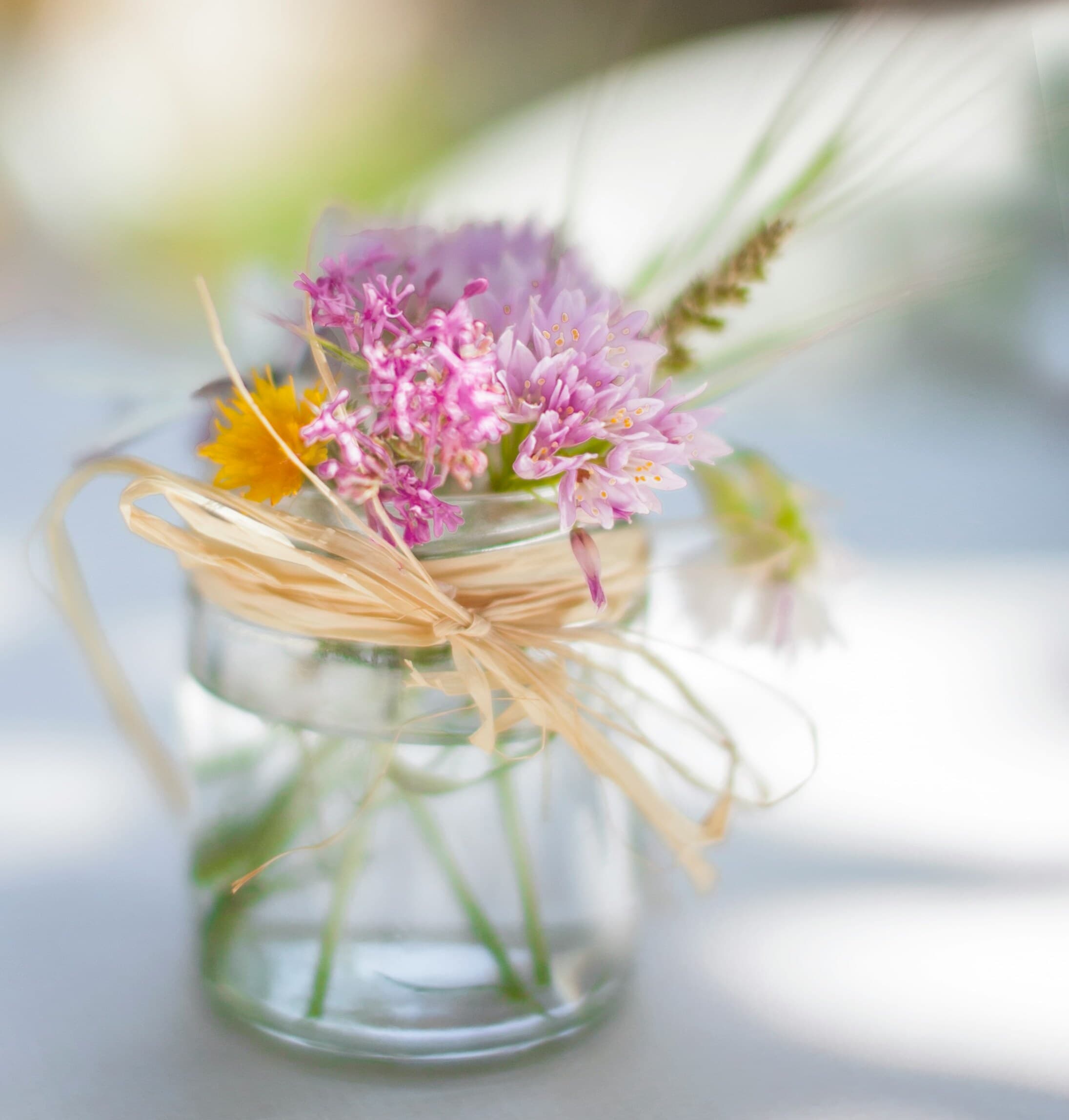 Small glass jar with a rustic twine bow, holding a bouquet of wildflowers on a sunlit table